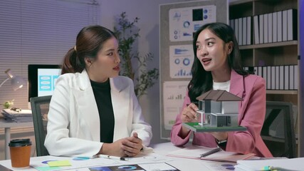 Professional architect presenting detailed house scale model to client during collaborative meeting, discussing design and construction specifics in modern office environment