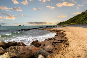 Sea shoreline with rocky breakwater and sunset sky with clouds