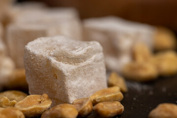 Turkish delight scattered on the table, sugar cubes with starch and toasted peanuts on a black slate surface, side view