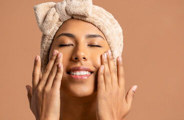 Smiling woman with towel on head touching face with closed eyes