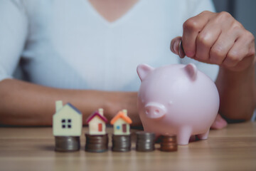Woman hand putting a coin into a piggy bank to save for a house. Saving money for a new home, property or real estate investment concept.
