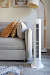 White tower fan against the background of a sofa with colorful pillows in a modern light interior