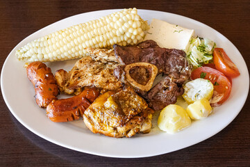 Ecuadorian roast served on a white plate, with a mix of meats like chicken, sausage, and beef, accompanied by corn, fresh cheese, sauced potatoes, and a tomato-lettuce salad. A flavorful Andean meal.