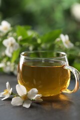 Tasty jasmine tea in cup and flowers on black table, closeup