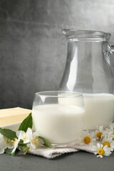Fresh dairy products and flowers on grey wooden table against textured background, closeup