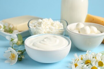 Fresh dairy products and flowers on light blue background, closeup