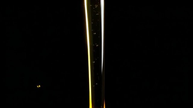 A viscous stream of golden liquid pouring slowly on a black background