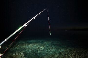 Point of view: Fishing in the blue ocean water at night. Lit by a flash. Fishing rod. Adriatic Sea