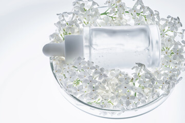 A bottle of serum in a petri dish with white flowers.