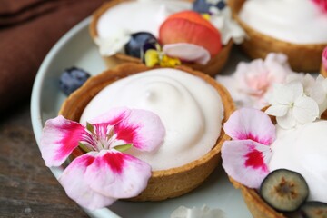 Delicious dessert. Tartlets with cream, berries and flowers on wooden table, closeup