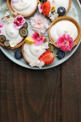 Delicious dessert. Tartlets with cream, berries and flowers on wooden table, top view. Space for text