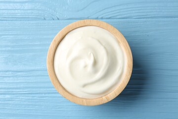 Tasty yoghurt in bowl on light blue wooden table, top view