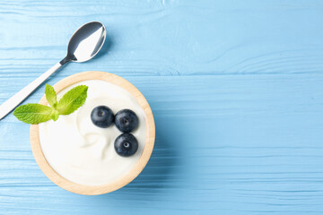 Tasty yoghurt with blueberries and mint in bowl on light blue wooden table, top view. Space for text