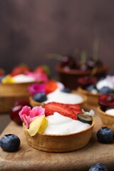 Sweet tartlets with berries and flowers on table against brown background, closeup. Delicious dessert