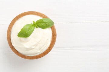 Delicious yogurt with basil in bowl on white wooden table, top view. Space for text