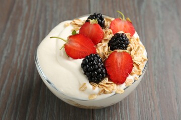 Tasty yogurt with granola and berries in bowl on wooden table, closeup
