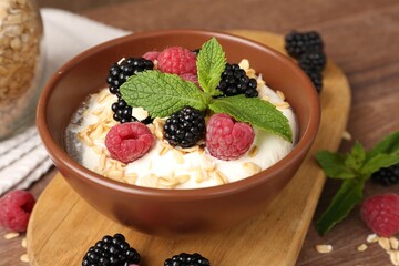 Tasty yogurt with granola and berries in bowl on wooden table, closeup