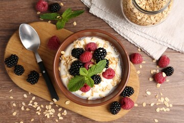 Tasty yogurt with granola and berries in bowl on wooden table, flat lay
