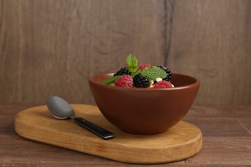 Tasty yogurt with granola and berries in bowl on wooden table, closeup