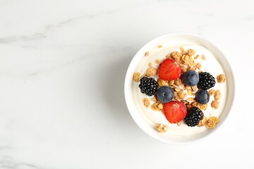 Tasty yogurt with granola and berries in bowl on white marble table, top view. Space for text