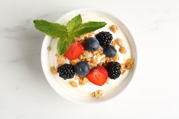 Tasty yogurt with granola and berries in bowl on white marble table, top view