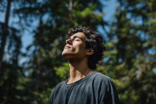 Young man enjoying peaceful moment outdoors with eyes closed, basking in sunlight surrounded by nature - Powered by Adobe