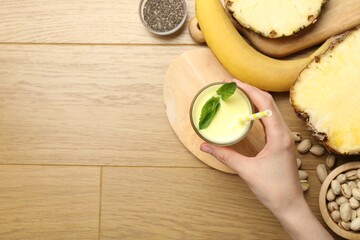 Superfood. Woman with tasty smoothie and ingredients at wooden table, top view. Space for text
