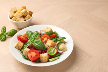 Delicious salad with croutons, vegetables and basil on wooden table, closeup. Space for text