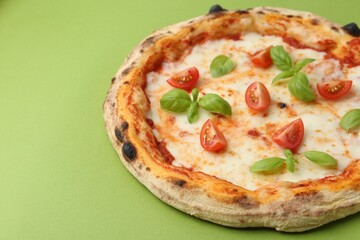 Delicious pizza with tomatoes and basil on green table, closeup