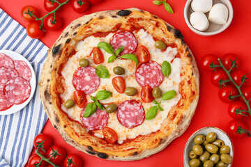 Delicious pizza and ingredients on red table, flat lay