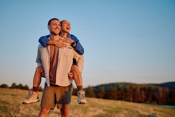 Young multiethnic couple laughing and enjoying piggyback ride in a field during a beautiful sunset