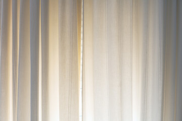 Sheer beige curtains with vertical stitching details softly illuminated by natural daylight. Minimalist interior decor with calming, warm tones.