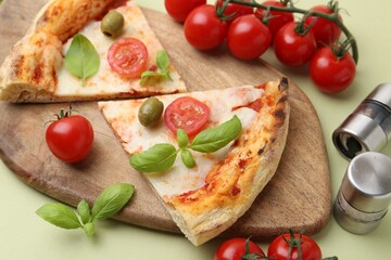 Pieces of delicious pizza, tomatoes and basil on light green background, closeup
