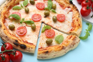 Delicious cut pizza with tomatoes, basil and olives on light blue background, closeup