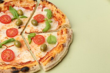 Delicious cut pizza with tomatoes, basil and olives on light green background, closeup. Space for text