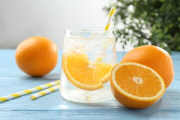 Sparkling water with orange slices in glass, fresh fruits and straws on light blue wooden table, closeup