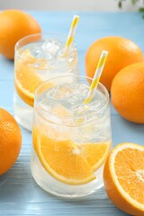 Sparkling water with orange slices in glasses and fresh fruits on light blue wooden table, closeup