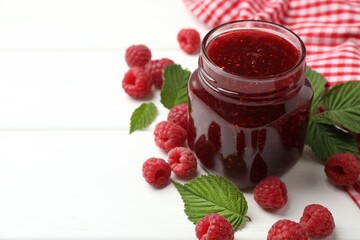 Tasty jam, fresh ripe raspberries and leaves on white wooden table, closeup. Space for text