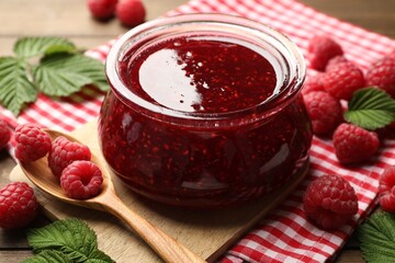 Tasty jam, fresh ripe raspberries and leaves on wooden table, closeup.