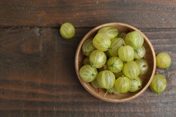 Fresh green gooseberries in bowl on wooden table, top view. Space for text