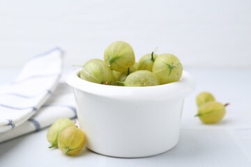 Fresh green gooseberries in bowl on white table, closeup