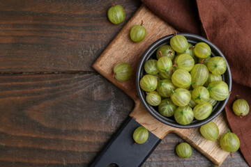 Fresh green gooseberries in bowl on wooden table, flat lay. Space for text