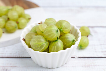 Fresh green gooseberries in bowl on white wooden table, closeup