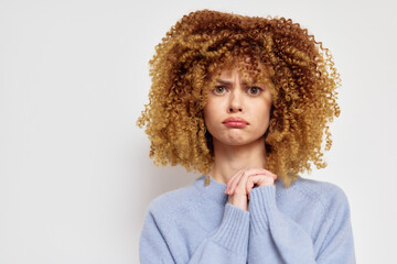 Sad woman with curly hair expressing disappointment, wearing a cozy blue sweater, set against a...