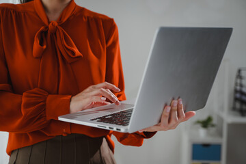 Businesswoman typing on laptop standing in office wearing red blouse