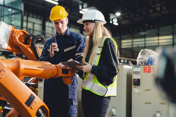 Industrial engineers collaborate in a high-tech factory environment, inspecting robotic machinery and discussing automation strategies with safety gear and real-time communication for precision