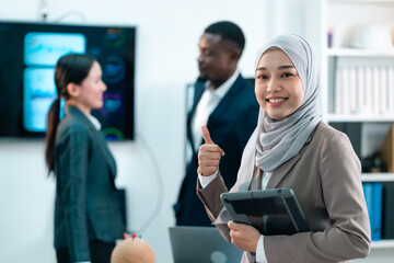 Confident Muslim businesswoman smiling and giving thumbs up while holding a tablet during a successful team meeting in a modern office environment showing leadership diversity and achievement