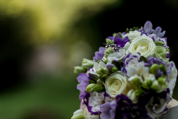 Wedding rings resting on purple and white bridal bouquet