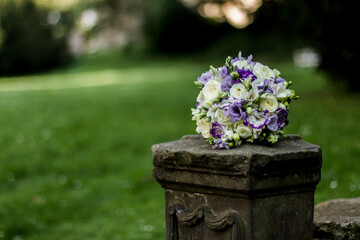 Wedding bouquet resting on stone pedestal in lush green garden