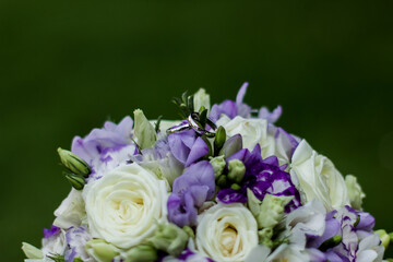 Wedding rings resting on beautiful bridal bouquet of white and purple flowers